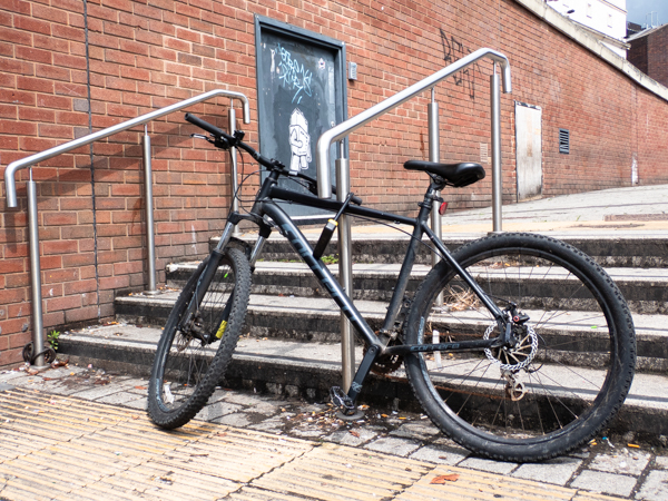 set of outdoor steps with a black bicycle leaning agains them a brick wall behind has some grafitti