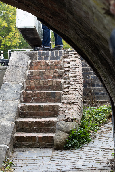 a set of stone steps leading up to a canal lock with a set of feet at the top and the arch of a bridge across the top right hand corner of the picture