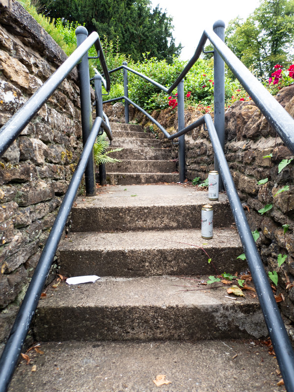 concrete steps with two empty larger cans and railings with old stone walls on either side