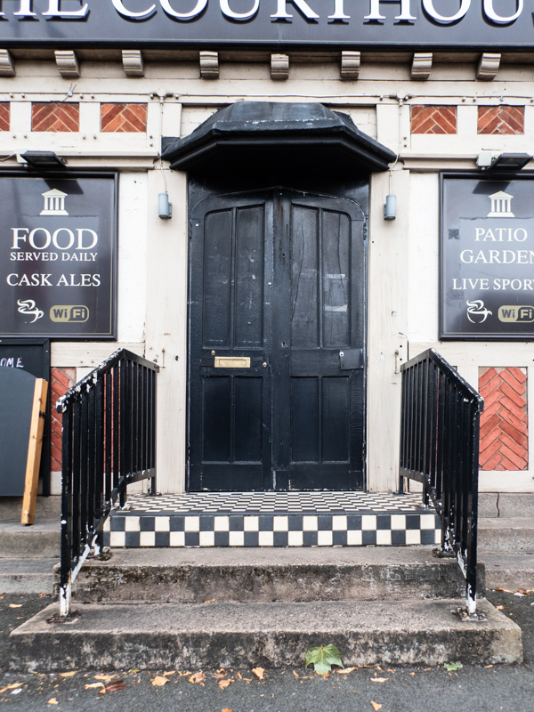 colour image of some black and white square tiled steps leading up to a black door.  The word courthouse is just visible above